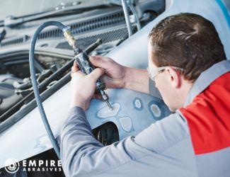 Auto body technician repairing car fender with abrasive on a pneumatic grinder