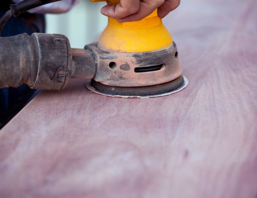 Closeup view of a person using a random orbital sander equipped with 5" sanding discs with VAC holes
